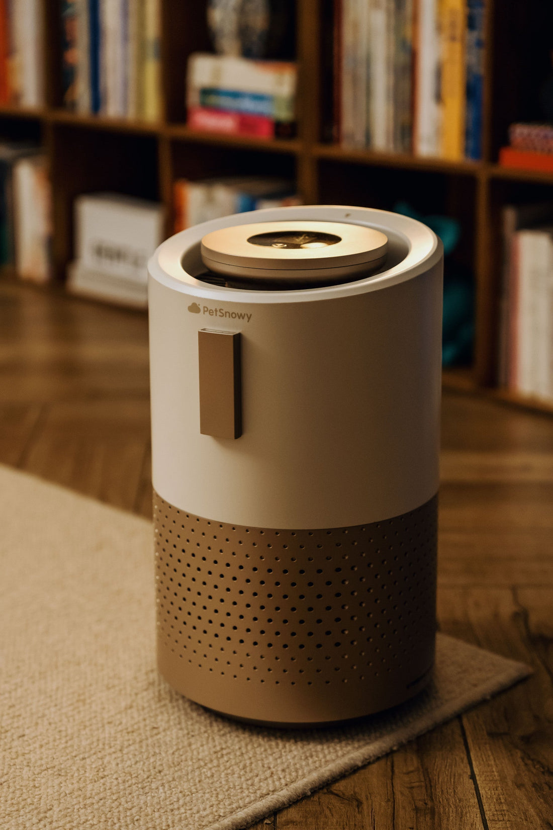 PetSnowy Air Purifier placed in a cozy modern living room with wooden flooring and bookshelves in the background.