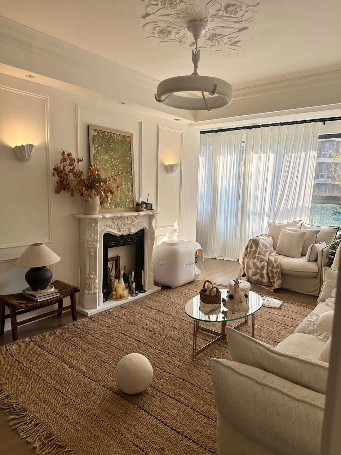 Cozy modern living room with white decor and a cat using a smart automatic litter box near the sofa